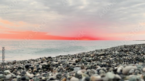 Calm waves at sunset. Wave splashing over pebbles at sea with foam. Rolling ocean waves. Summer paradise beach background at sunset