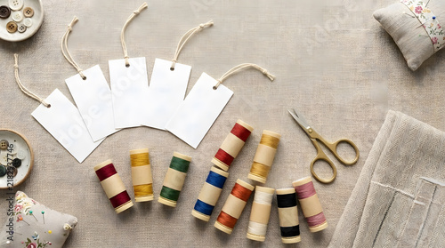 Blank white hang tags mockup on linen fabric with colorful sewing thread spools and scissors for sustainable fashion and handmade branding.