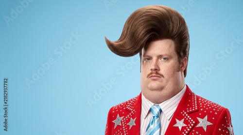Funny eccentric man with exaggerated retro pompadour hairstyle and flamboyant red star suit posing against a blue background