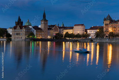 Картината върху платно Evening view of Prague with buildings, reflections, and a boat on the water