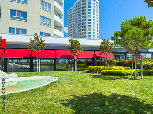 Green space with bushes and water feature near tall buildings on a sunny day in a city park setting