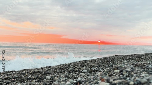 Calm waves at sunset. Wave splashing over pebbles at sea with foam. Rolling ocean waves. Summer paradise beach background at sunset