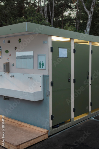 Bild auf Leinwand Mobile sanitary unit with a long wash trough and green cubicle doors lit from inside, standing on a wooden ramp at a field camp