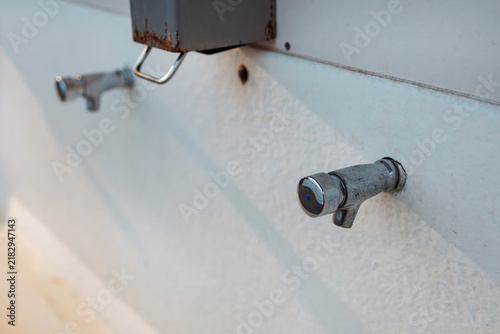 Konstfotografi Row of chrome push taps and a soap dispenser on the white wall of a temporary field washroom, shot with shallow depth of field