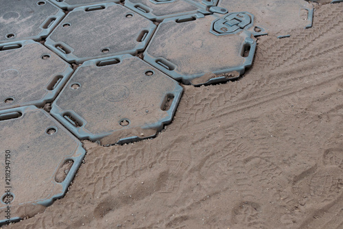 Fotografie The edge of a temporary trackway meets bare sand marked with boot prints and tyre tracks at a military camp