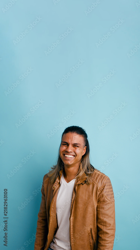 Fototapeta premium Cheerful latino man wearing a leather jacket, looking at camera and smiling with happiness in a studio setting