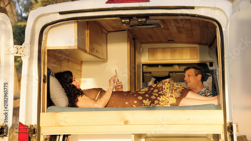 Mature couple relaxing on a bed inside a customized camper van, enjoying the van life freedom and travel adventure