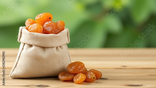 Small beige fabric pouch filled with dried apricots on a wooden surface, natural food, healthy snack, organic fruit, rustic presentation, close-up