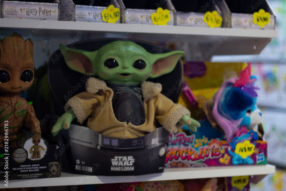 Obraz premium Horizontal photo. Grogu Yoda doll from Star Wars Mandalorian on toy store shelf with other toys. Green alien character action figure in packaging. Merchandise, pop culture, kids games, retail shopping