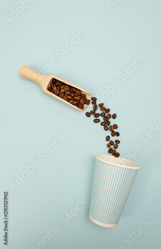 Business-oriented photo of beans entering paper cup from scoop, taken top down on blue background for ad use