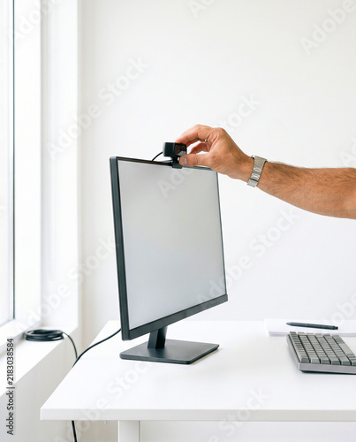 Hand Adjusting Webcam on Top of Computer Monitor on Office Desk
