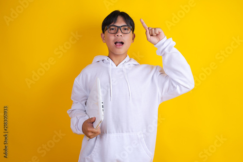 Konstfotografi Asian Teen Boy Pointing Finger up With Excited Idea Expression Holding Laptop