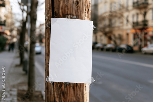 Blank white paper flyer taped to a wooden utility pole on a city street