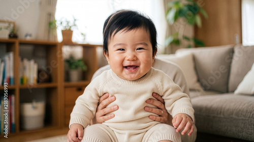 Cheerful Asian baby sitting on parent lap in a living room