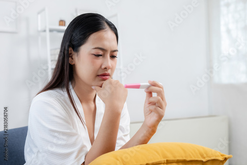 Obraz na plátně Asian women looking worried while holding home pregnancy test, representing pregnancy testing, fertility, reproductive health, uncertainty, family planning, important life decision
