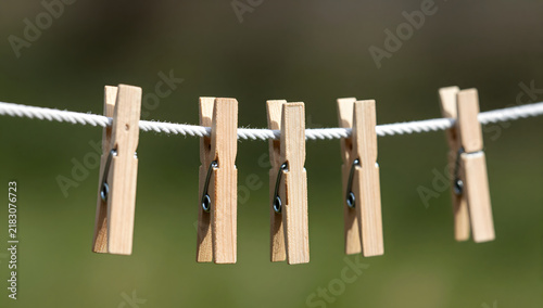 Wooden Clothespin Line: A series of simple wooden clothespins are attached to a taut clothesline, waiting to hold laundry, set against a softly blurred green background.