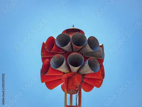 Obraz na plátně Close-up low angle view of a vintage red multi-horn civil defense tornado emergency warning siren against a clear blue sky