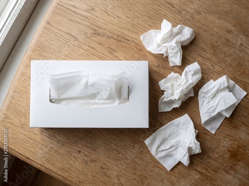 White tissue box with crumpled tissues on a wooden surface