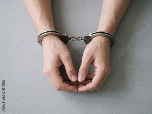 Close up of arrested human hands in steel handcuffs on gray surface