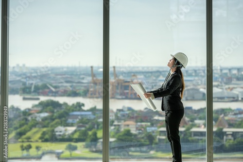 architect woman reading blueprint thinking planning project interior on empty office interior near glass window. office architect standing reading blueprint on skyscraper floor construction workplace