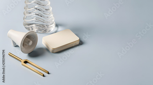 Sound Science Setup: A tuning fork, a small megaphone, and a glass of water are arranged on a light blue surface, hinting at an exploration of acoustics and sound wave principles.