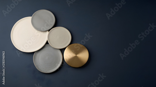 Modern Plate Arrangement: A minimalist composition of ceramic and metal plates in various neutral tones and finishes, artfully arranged on a dark, textured background.