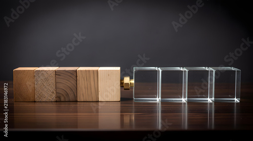 Contrast of Materials: A juxtaposition of solid wooden blocks and transparent acrylic cubes sits on a polished wooden surface, representing the interplay between natural and manufactured elements.