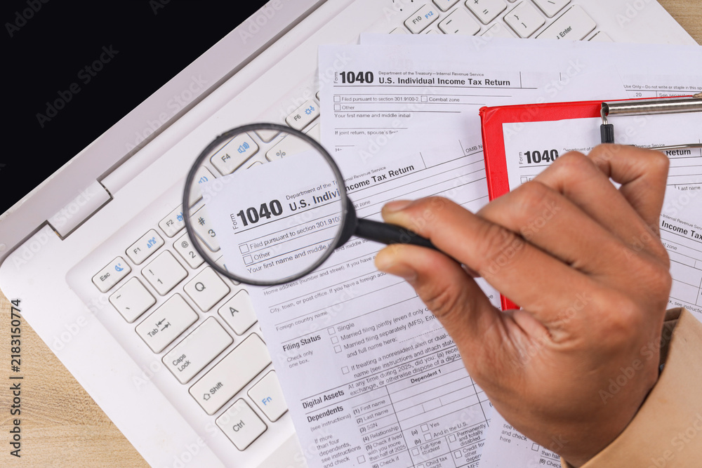 Obraz premium Closeup of Hand Holding Magnifying Glass for US Individual Income Tax Return Form 1040 on Laptop