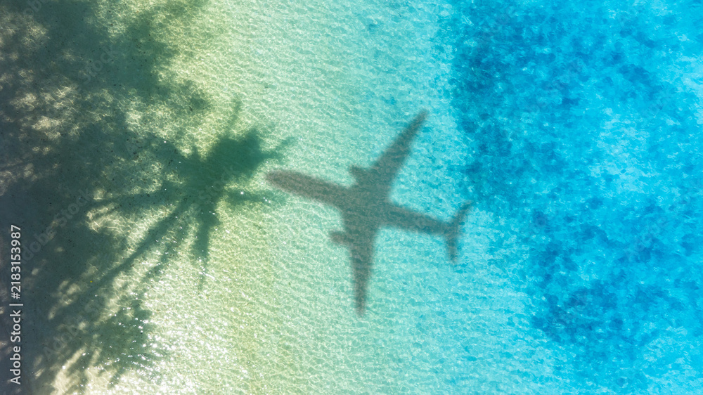 Obraz premium Aerial view of shadow passenger plane silhouette and sandy beach blue sea with waves at sea beach summer vacation sea travel concept 