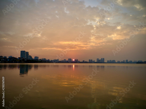 Peaceful City Skyline Across a Calm Lake at Sunset Under Dramatic Golden Clouds and Reflective Evening Water on West Lake in Hanoi, Vietnam