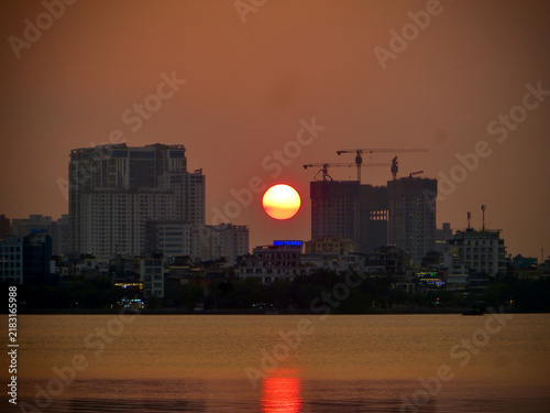 Close-Up Sunset Behind High-Rise Buildings and Construction Cranes on West Lake in Hanoi, Vietnam