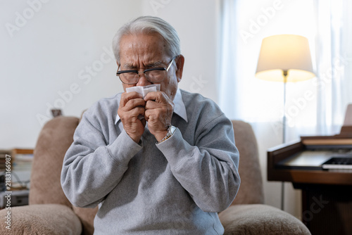 Fotografía Uncomfortable senior asian man sneezing into tissue feeling sick with cold or fl