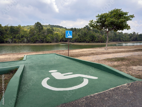 Wheelchair accessible ramp with disability symbol near lakeside, barrier-free access in natural outdoor setting, inclusivity and accessibility concept, wheelchair logo, public street, national park
