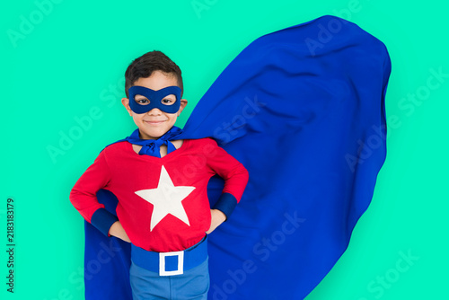 Fotografie Child in superhero costume with red shirt and blue cape on teal background