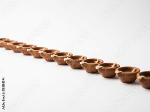 A Row of Miniature Earthen Diyas Lined Up on a White Surface