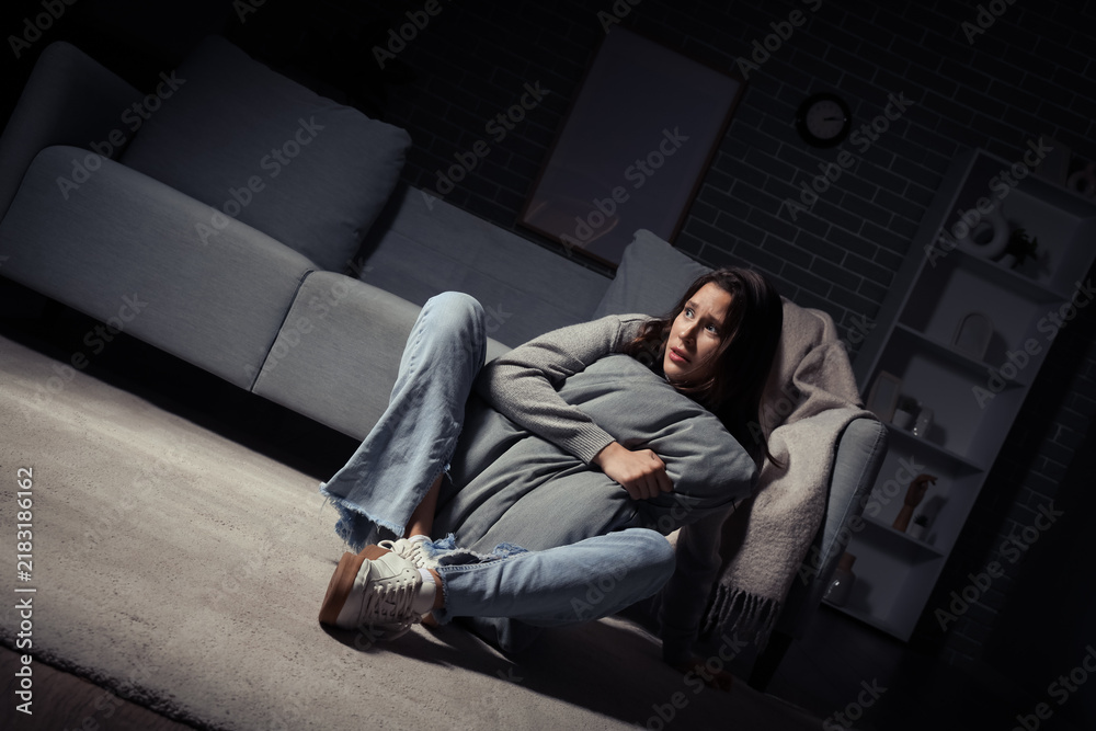 Fototapeta premium Scared young woman with cushion sitting at home