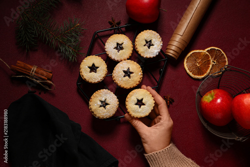 Fotografía Female hand with tasty Christmas mince pies, fresh apples and spices on red back