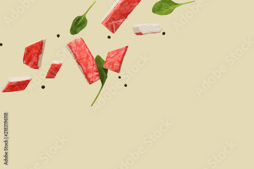 Obraz na płótnie Cut tasty crab sticks with peppercorns and spinach leaves flying on green backgr