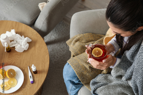Ill young woman with cup of lemon tea sitting in armchair at home, closeup
