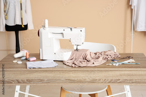 Фотография Modern sewing machine with beige fabric and tailors supplies on table in atelier