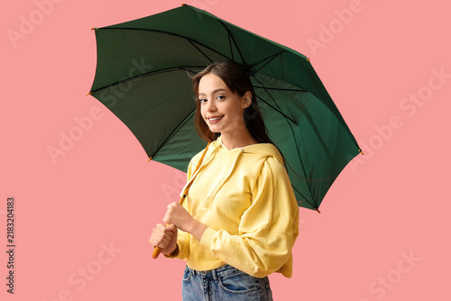 Beautiful young woman with green umbrella on pink background