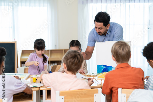 Caucasian male teacher teaching art lesson to children in classroom. 