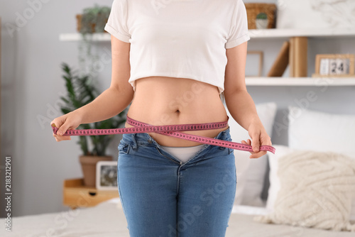 Young woman in tight jeans measuring her belly at home  closeup. Weight gain concept