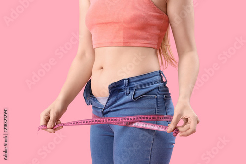 Young woman in tight jeans measuring her hips on pink background, closeup. We...