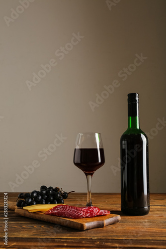 Obraz na płótnie Bottle and glass of red wine with snacks on wooden table against white backgroun