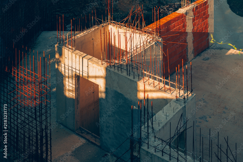 Obraz premium High-angle view of cast concrete walls and exposed steel rebar on a building construction site in warm sunlight.