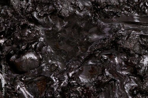 Dark surface with shiny texture found in a natural setting, possibly related to oil or tar deposits