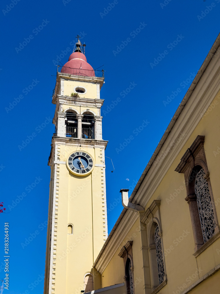 Fototapeta premium Yellow church clock tower with red dome and arched windows under blue sky in Corfu, Greece