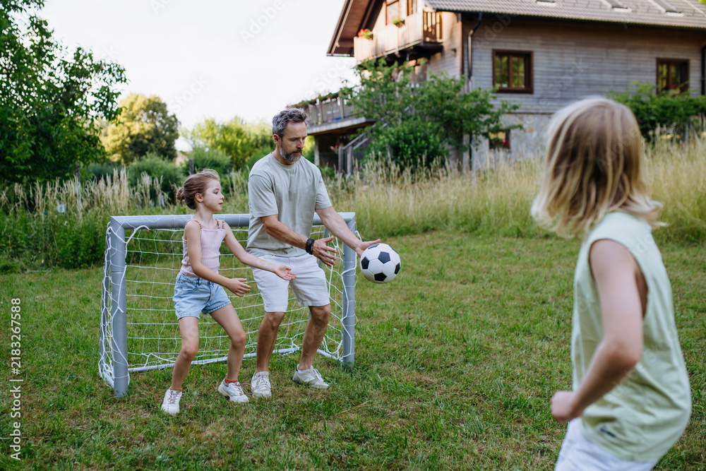 Obraz premium Father and kids playing football in backyard during summer afternoon.