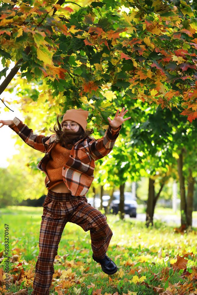 Obraz premium Joyful Girl Playing in Autumn Leaves Wearing Orange and Brown Plaid Outfit